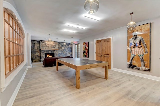 rec room featuring a stone fireplace and light hardwood / wood-style flooring