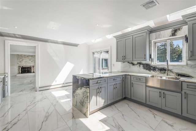 kitchen with a stone fireplace, decorative backsplash, gray cabinets, a baseboard radiator, and kitchen peninsula