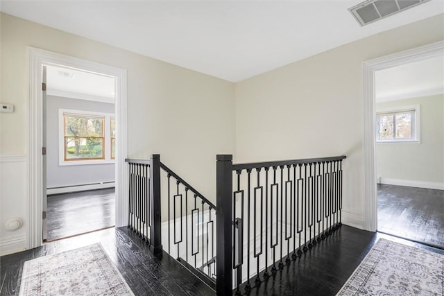 stairs featuring baseboard heating, a healthy amount of sunlight, and wood-type flooring