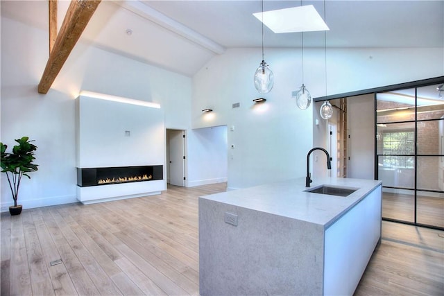 kitchen with pendant lighting, sink, beam ceiling, an island with sink, and light wood-type flooring