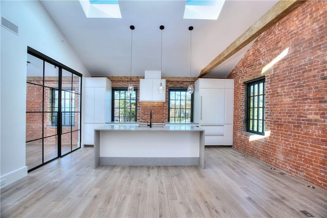 kitchen featuring a skylight, white cabinetry, an island with sink, and decorative light fixtures