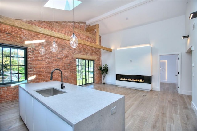 kitchen with pendant lighting, sink, white cabinetry, a wealth of natural light, and brick wall