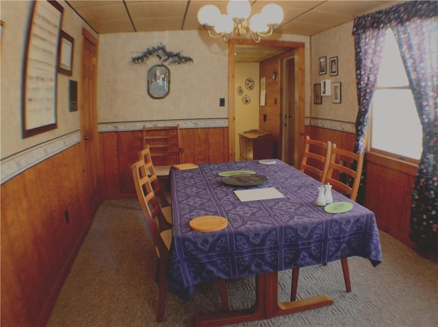 carpeted dining space with a paneled ceiling, wood walls, and a chandelier