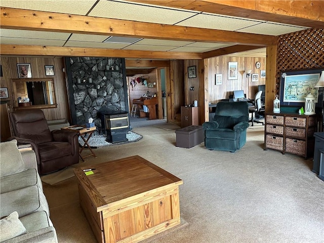 carpeted living room with wood walls, a wood stove, and beam ceiling