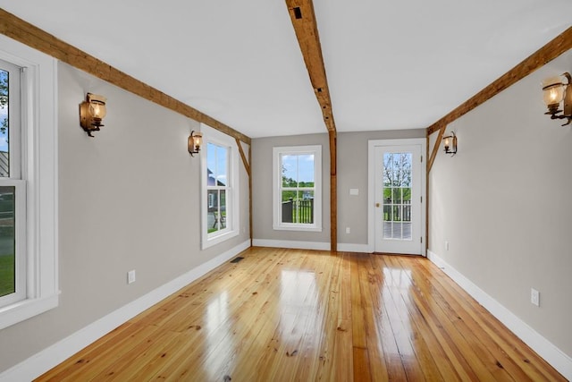 unfurnished living room with beamed ceiling and light wood-type flooring