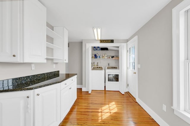 kitchen with washing machine and dryer, light hardwood / wood-style floors, white cabinetry, and dark stone countertops