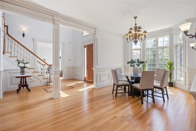 dining space featuring ornate columns, ornamental molding, a notable chandelier, and light wood-type flooring