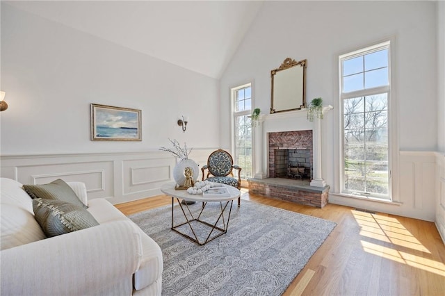 living room featuring light wood-type flooring, high vaulted ceiling, and a brick fireplace