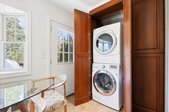 clothes washing area featuring stacked washer and dryer, ornamental molding, laundry area, and a healthy amount of sunlight