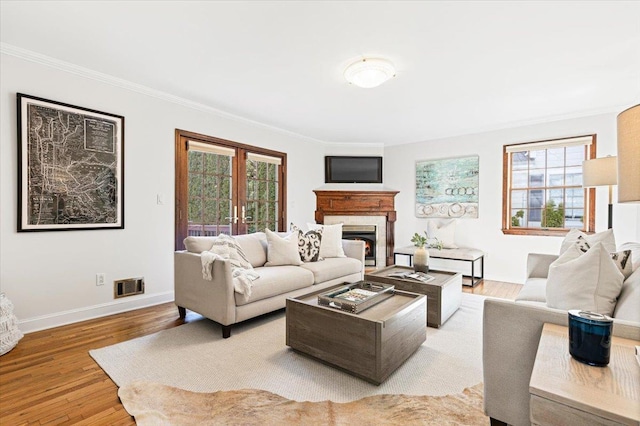 living area with crown molding, visible vents, a glass covered fireplace, light wood-type flooring, and baseboards