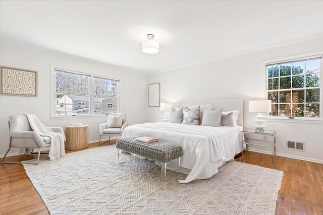 bedroom featuring ornamental molding, visible vents, baseboards, and wood finished floors