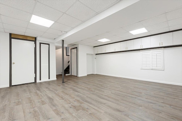 finished basement featuring a drop ceiling, light wood-type flooring, and baseboards