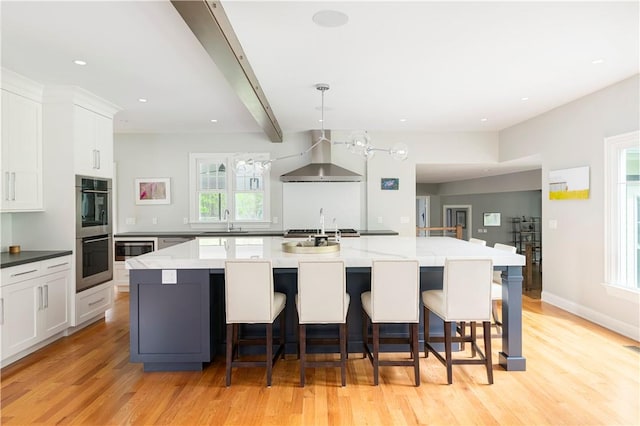 kitchen featuring a large island with sink, a wealth of natural light, and wall chimney exhaust hood