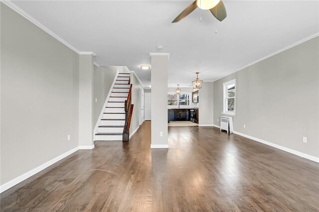 unfurnished living room featuring ceiling fan with notable chandelier, dark hardwood / wood-style flooring, and crown molding