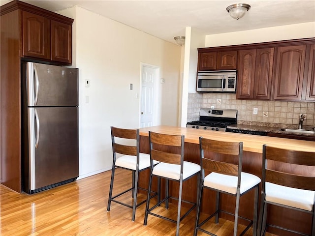 kitchen featuring light wood-type flooring, butcher block counters, stainless steel appliances, and tasteful backsplash