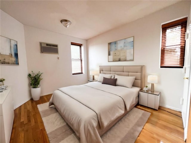 bedroom featuring a wall mounted air conditioner, light wood-type flooring, and multiple windows