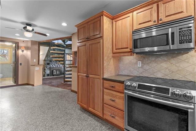 kitchen with ceiling fan, a fireplace, appliances with stainless steel finishes, and tasteful backsplash