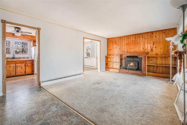 unfurnished living room featuring ceiling fan, a baseboard heating unit, carpet flooring, and wooden walls