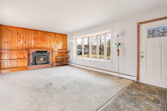 unfurnished living room featuring a wood stove, a baseboard heating unit, wood walls, and dark carpet