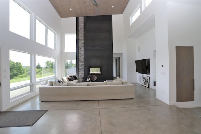 living room featuring a stone fireplace, a towering ceiling, and concrete floors