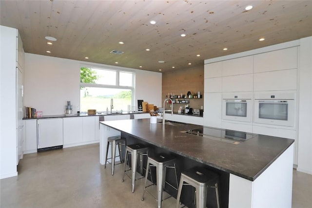 kitchen featuring stainless steel stovetop, oven, a spacious island, sink, and white cabinetry