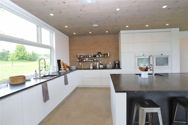 kitchen featuring dark stone countertops, wood walls, sink, and white cabinets