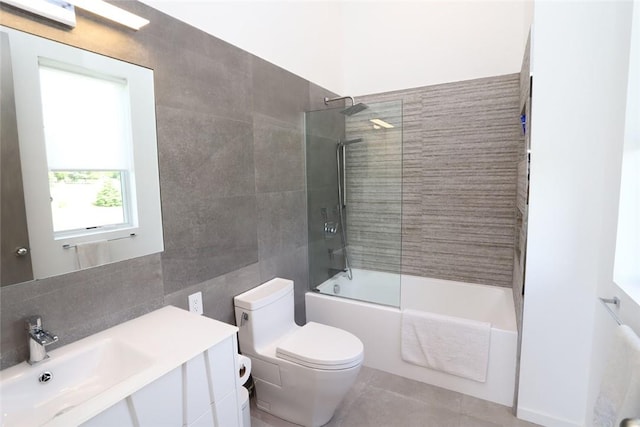 full bathroom with vanity, tile patterned floors, tiled shower / bath, toilet, and tile walls