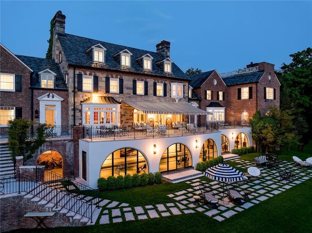 back house at dusk with a yard, a balcony, and a patio