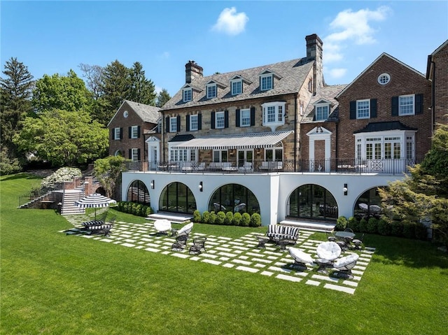 rear view of property with a yard, a balcony, and a patio