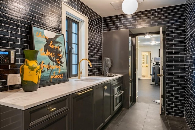 bar with dark tile patterned floors, sink, stainless steel oven, and brick wall