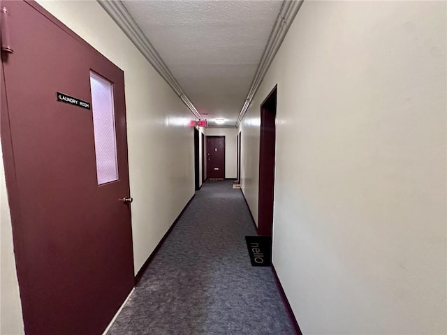 hallway featuring dark colored carpet, ornamental molding, and a textured ceiling