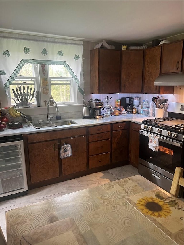 kitchen with dark brown cabinetry, sink, beverage cooler, and stainless steel range with gas stovetop