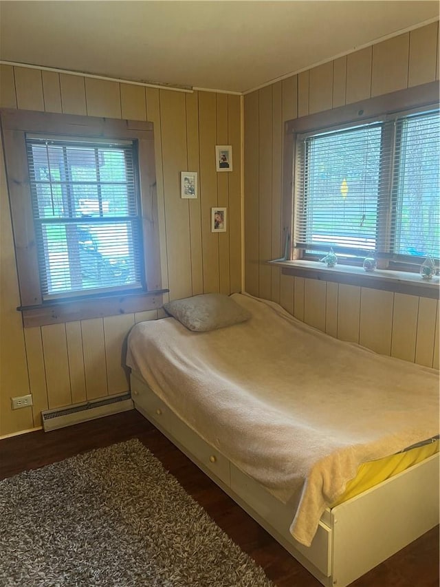 bedroom with wooden walls, baseboard heating, and dark wood-type flooring