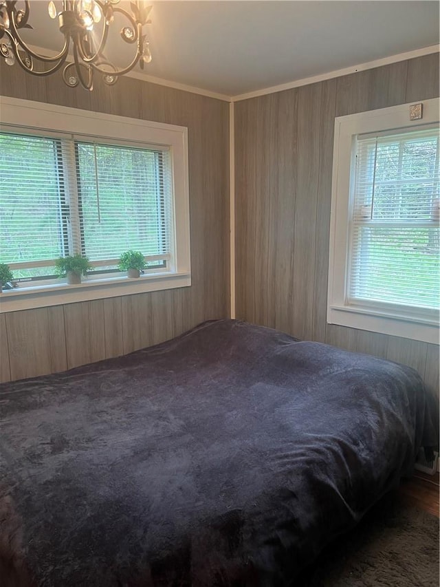 unfurnished bedroom with dark carpet, ornamental molding, wooden walls, and an inviting chandelier