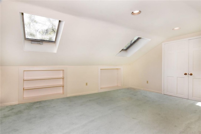 bonus room featuring built in shelves, light carpet, and vaulted ceiling with skylight