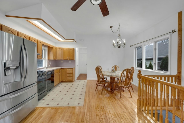 kitchen featuring appliances with stainless steel finishes, ceiling fan with notable chandelier, sink, decorative light fixtures, and light hardwood / wood-style flooring