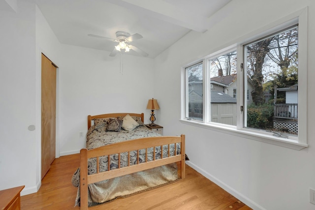 bedroom with beam ceiling, light hardwood / wood-style floors, and ceiling fan