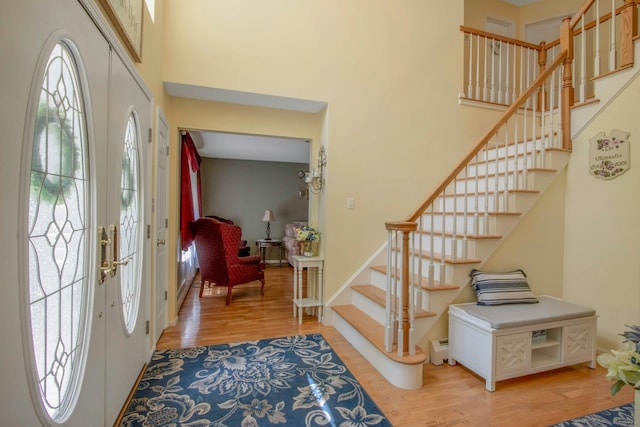 entryway with a high ceiling, light wood finished floors, stairs, baseboard heating, and baseboards
