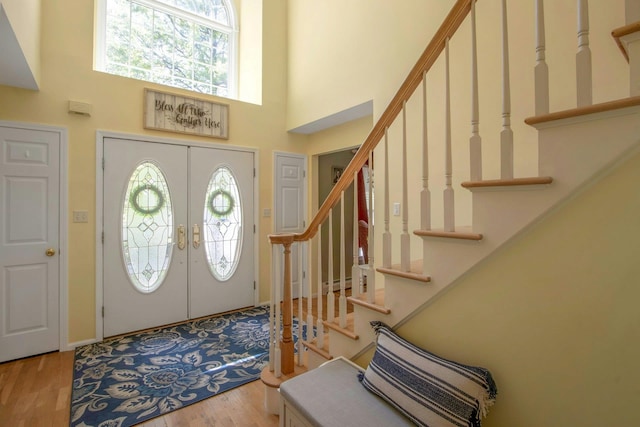 foyer entrance with stairs, a towering ceiling, wood finished floors, and french doors