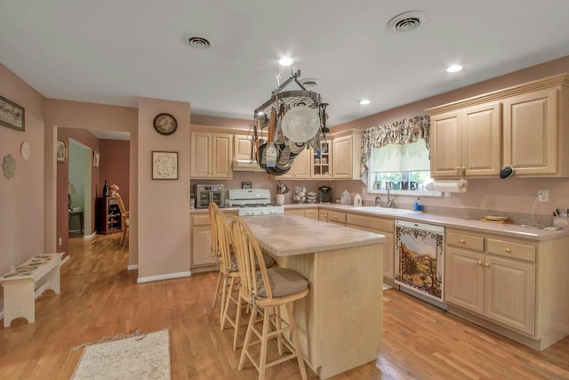 kitchen with a sink, dishwashing machine, light countertops, white range with gas cooktop, and a breakfast bar