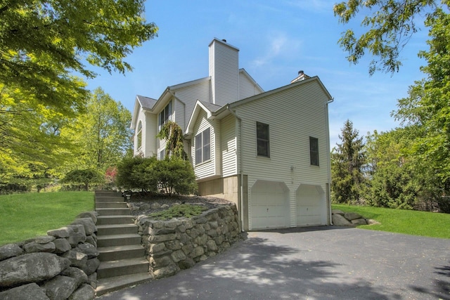 view of home's exterior with a garage, driveway, a chimney, and a yard