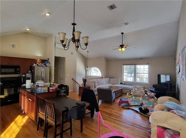 dining area featuring ceiling fan with notable chandelier, light hardwood / wood-style floors, and vaulted ceiling