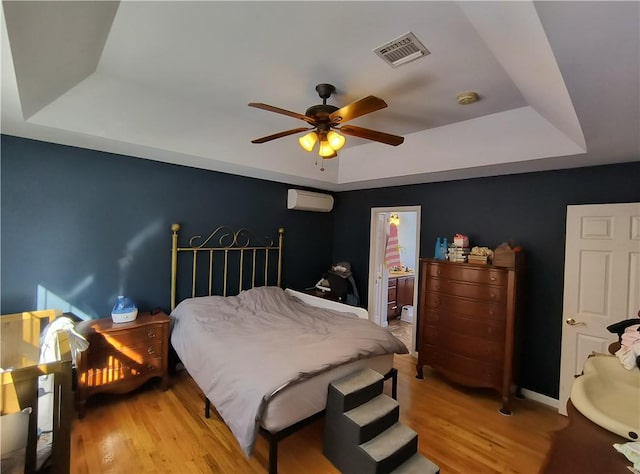 bedroom with connected bathroom, ceiling fan, a raised ceiling, an AC wall unit, and hardwood / wood-style flooring