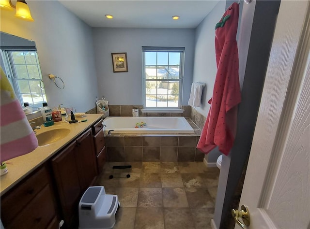 bathroom featuring vanity, toilet, and tiled bath