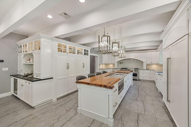 kitchen with a kitchen island, white cabinets, hanging light fixtures, and wood counters