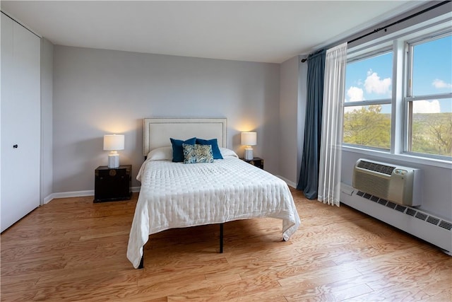 bedroom featuring a closet, a baseboard radiator, a wall mounted air conditioner, and light wood-type flooring