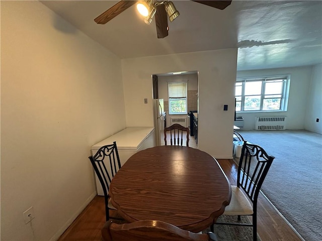 dining space with ceiling fan, radiator heating unit, hardwood / wood-style floors, and vaulted ceiling