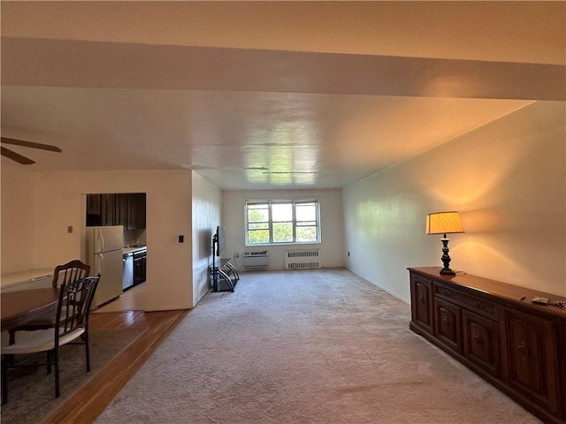 living room with light carpet, radiator heating unit, a wall mounted AC, and ceiling fan