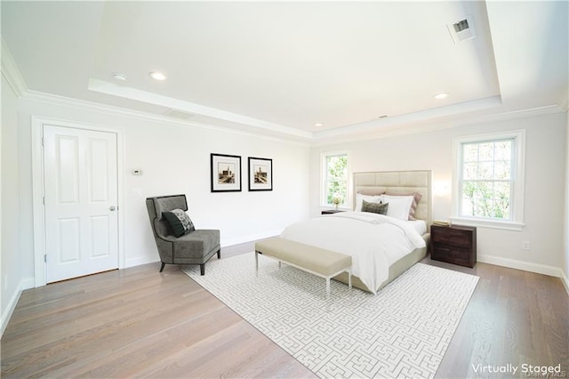 bedroom with hardwood / wood-style flooring, a tray ceiling, and multiple windows