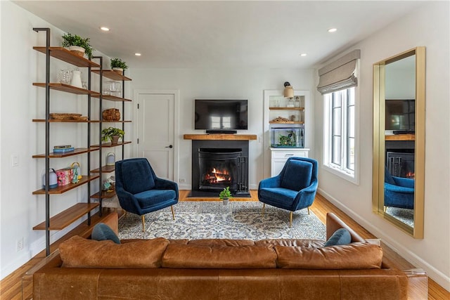 living room featuring recessed lighting, a fireplace with flush hearth, and wood finished floors